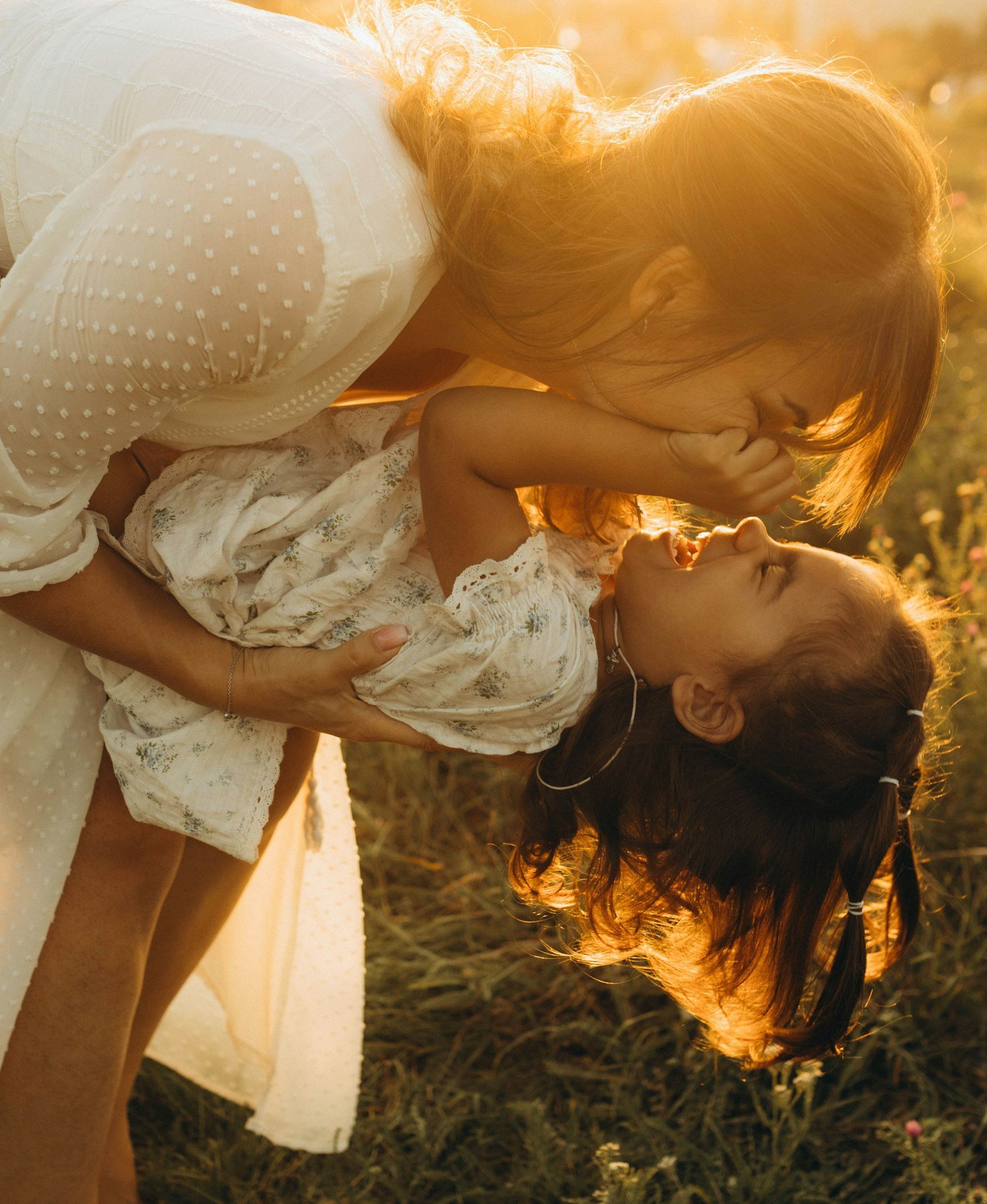 A mother lifting her laughing daughter in a golden field
