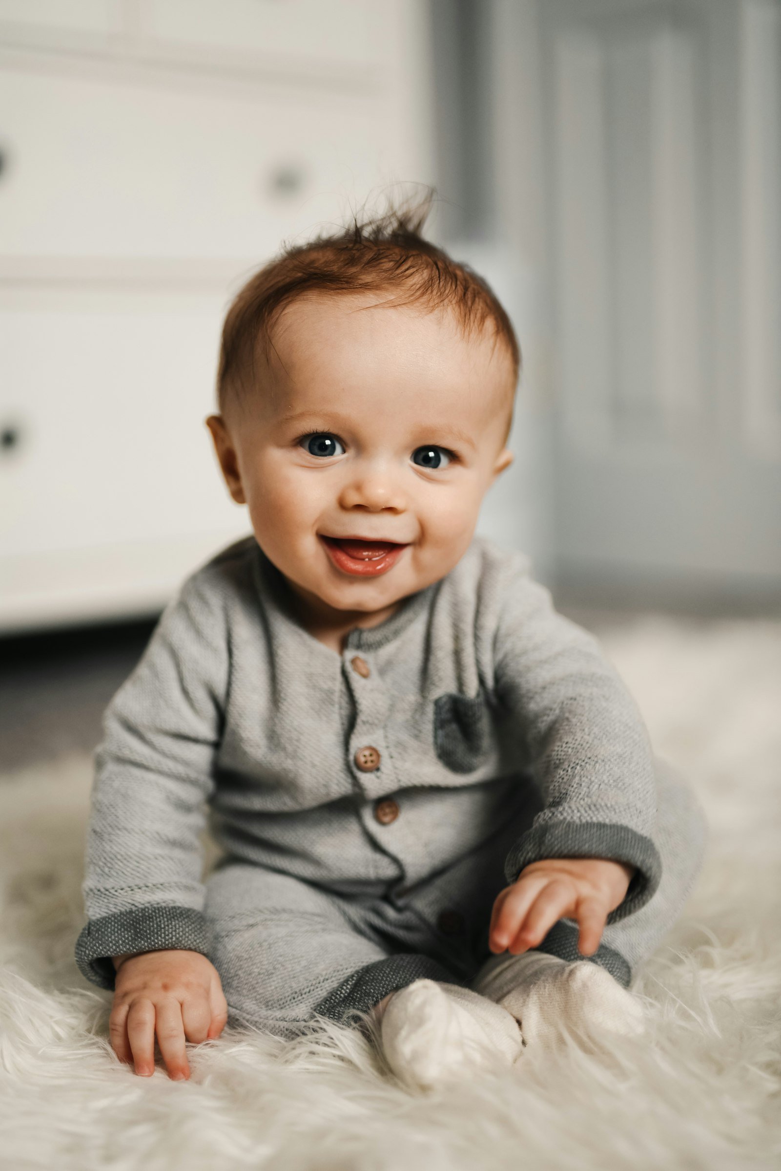 A smiling baby sitting on a soft white rug
