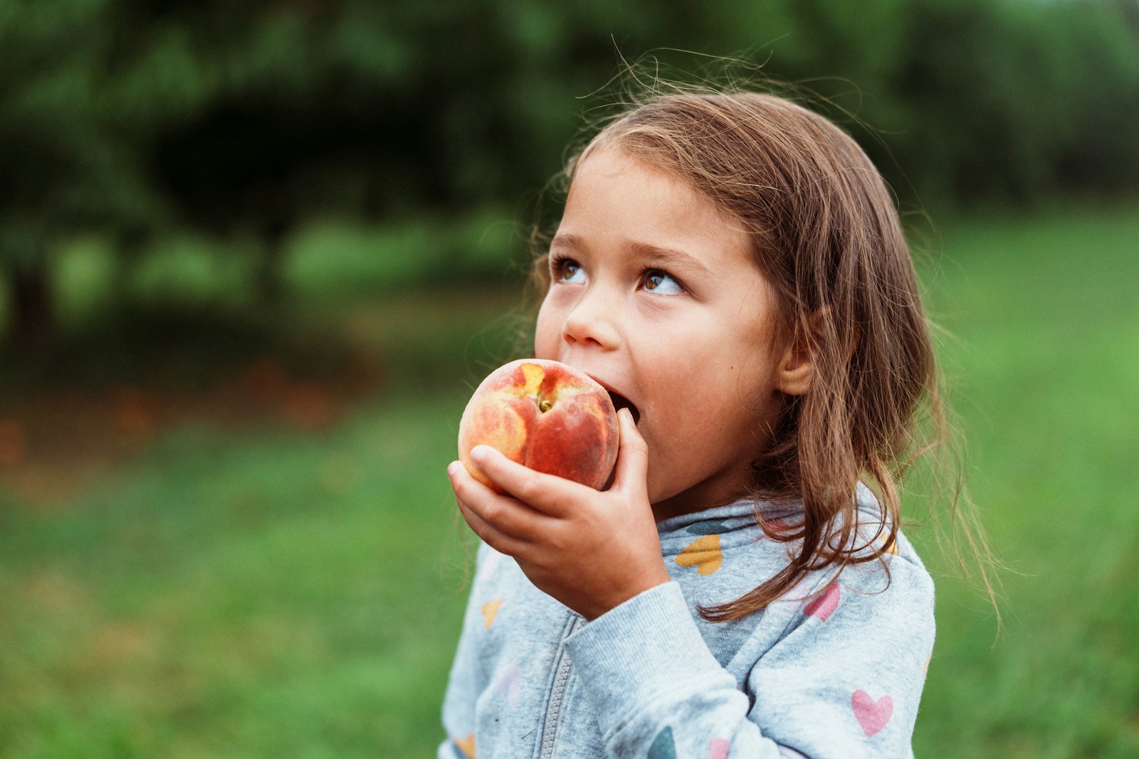 A young girl biting into a fresh peach outdoors
