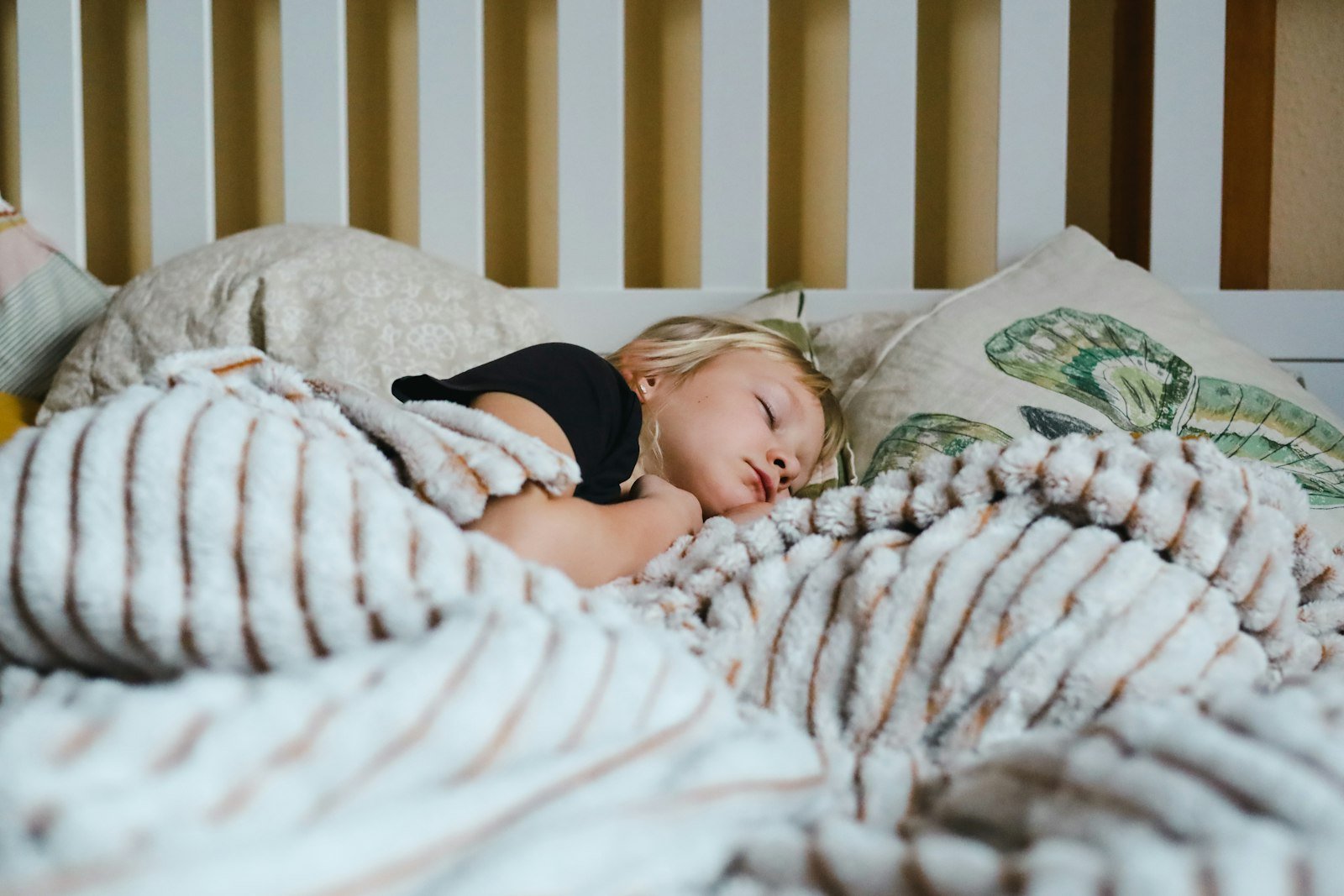 A child sleeping peacefully under a soft striped blanket